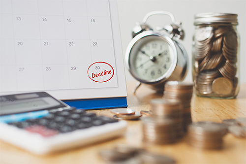 Close up of a table with coins, calculator and calendar showing a red deadline for the end of the month