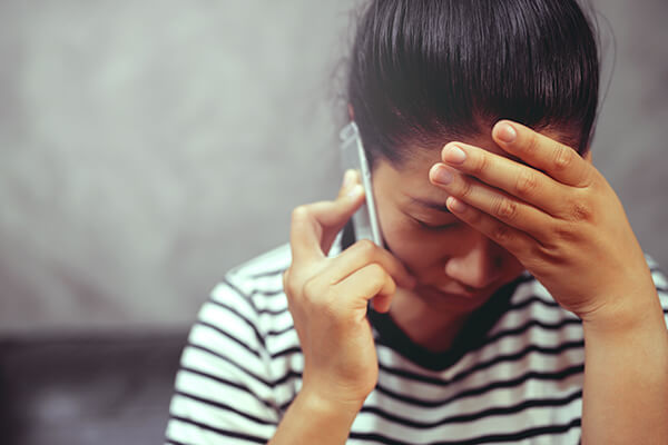 Anxious brunette woman having frustrated stressed expression, holding one hand on her head and a phone with her other one