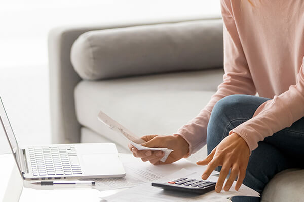 Hand woman calculating expenses on a calculator with bills and a computer