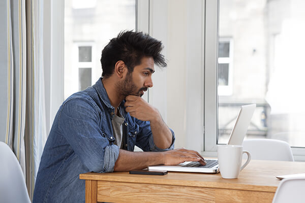 Young guy sitting on his desk and looking at his laptop