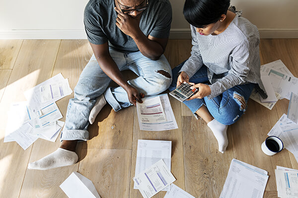 Couple sitting on the floor with a calculator, with a lot of bills around them 