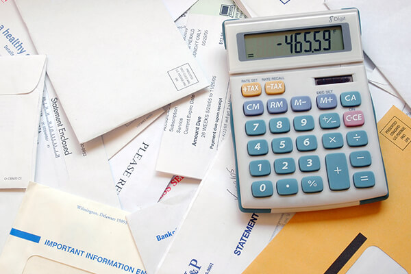 Close up of a table full of letters and bills, with a calculator on it 