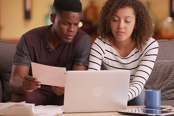 A couple reviews their debt consolidation options while sitting on a couch with a laptop.