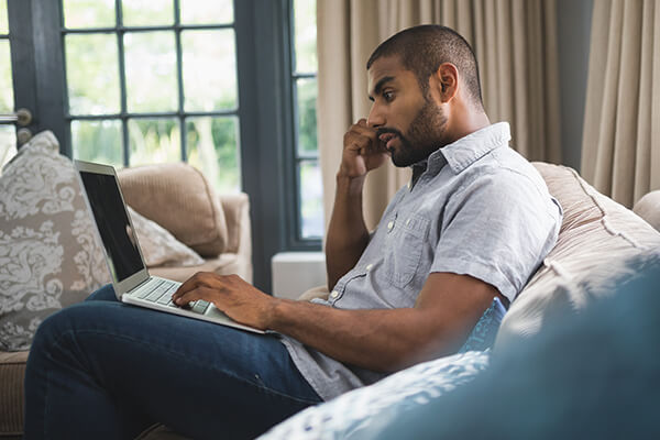 A man sits on his couch, browing resources related to financial assistance and debt relief. 