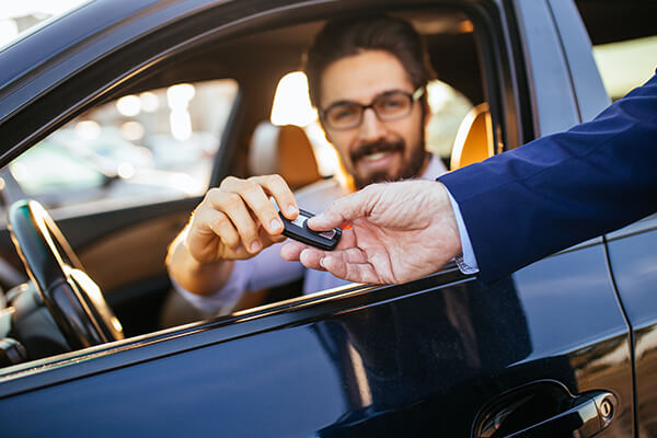 A man in the front seat of a car accepts the keys to his new car.  