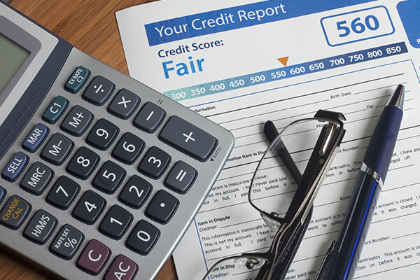 Close up of a table with a credit score report sheet, glasses, calculator and pen. 