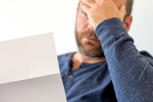 Close up of a man holding is head while looking at a letter