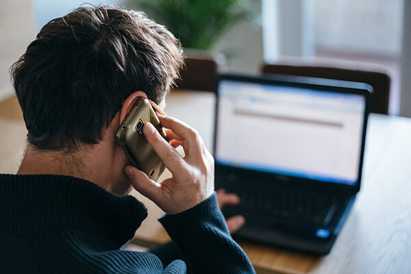 Back shot of a man using computer while speaking on the phone 