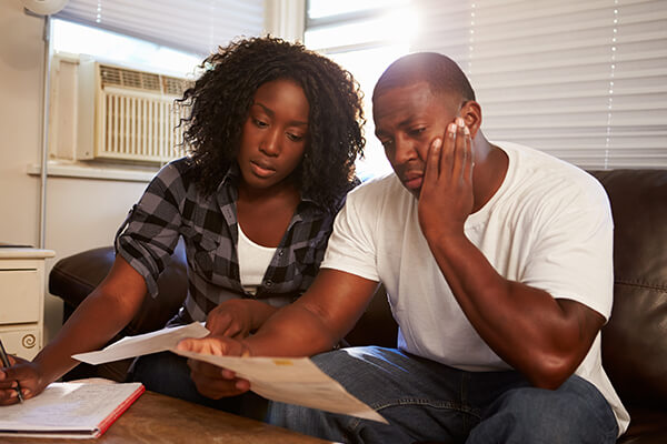 Anxious couple sitting on their couch reading their bills at home in living room