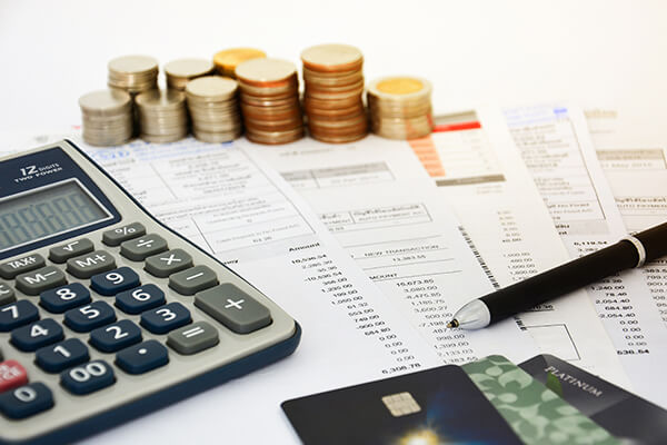 Close up of bills with calculator, stack of coins, pen and credit cards