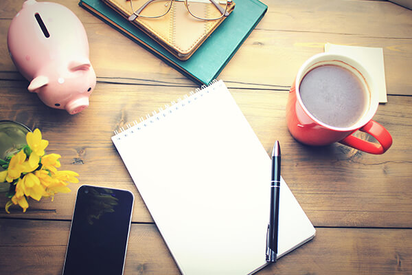 A budget and spend tracking notebook beside a copy of coffee and a phone. 