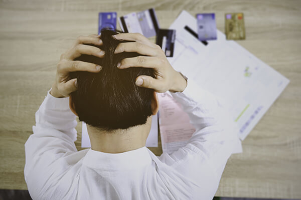 Man holding his head looking at multiple credit cards on the table