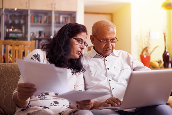 A couple with bills and financial documents on a laptop looking at their budget and responding to a creditor call.