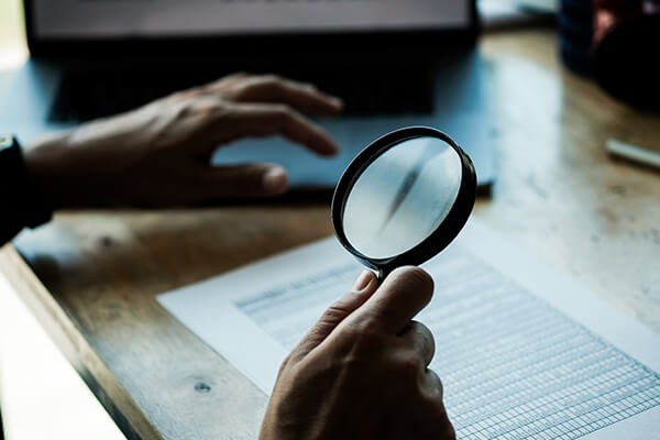 A person holds a magnifying glass over an expense tracking spreadsheet.