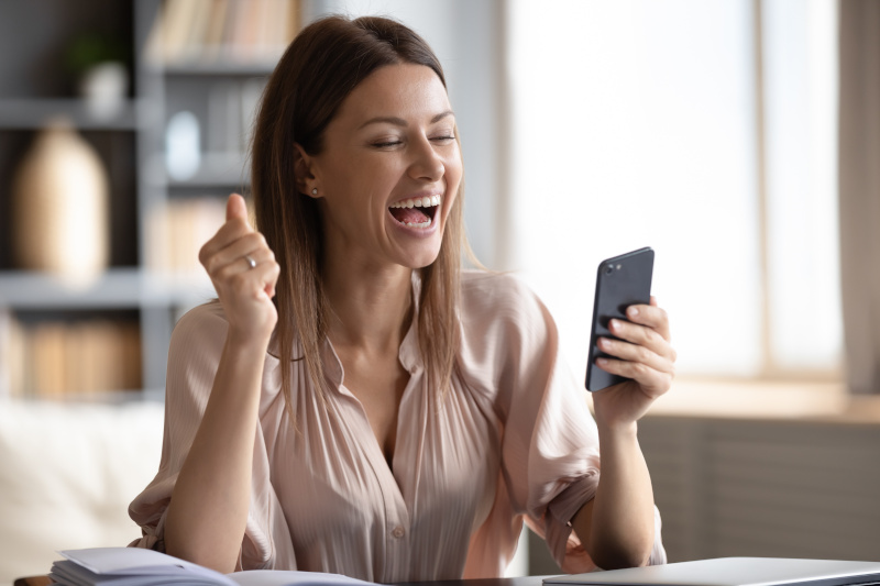 A woman is excited and feeling rewarded looking at information on her phone after paying off some of her debt.