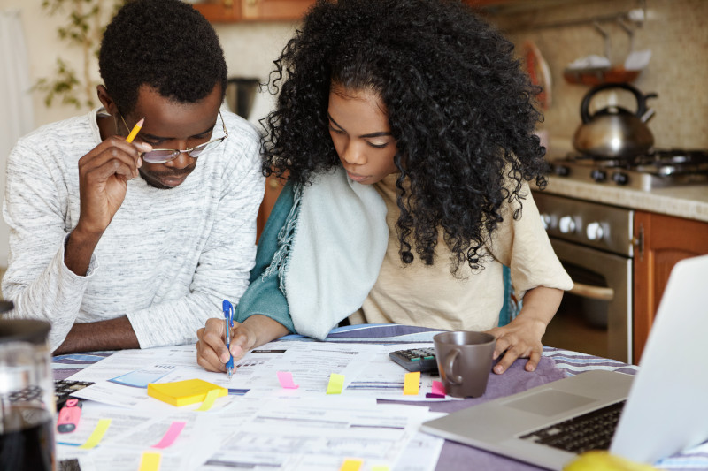 A couple with bills, bank statements, a calculator, and laptop planning out their family budget.