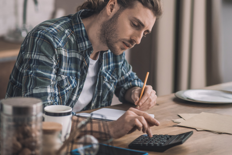 A man sitting at his kitchen table budgeting money at home.