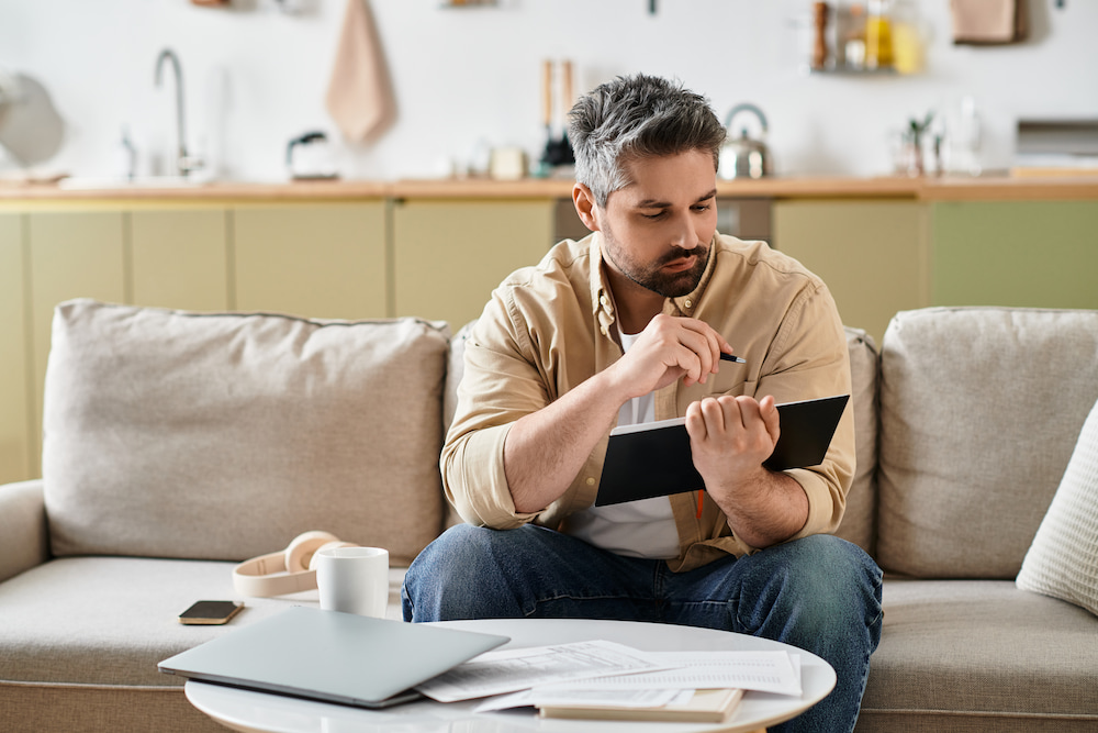 A man at home sitting on his couch  trying to decide between paying debt and investing.